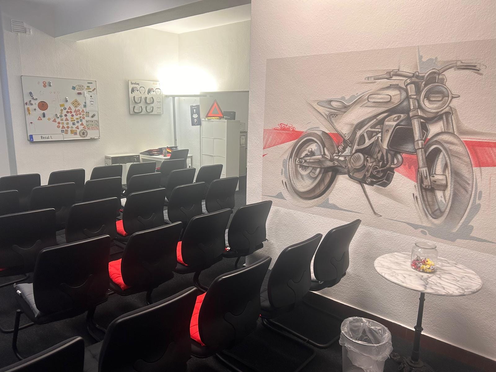 Theorieraum mit Verkehrszeichen-Magnettafel, Reifenprofil-Schautafel und dem Motorrad-Wandbild daneben.